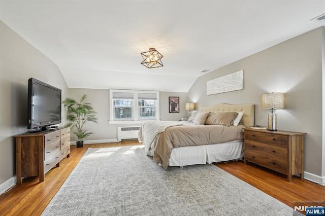 bedroom with light wood-style flooring, radiator, baseboards, and lofted ceiling