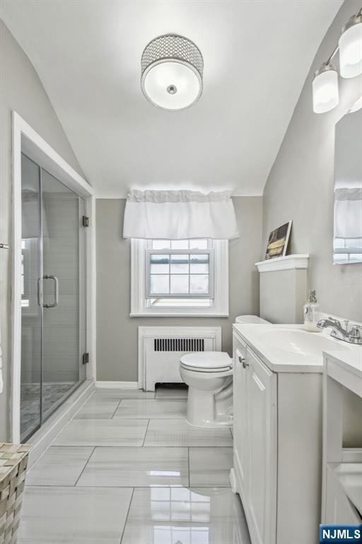 bathroom featuring toilet, radiator heating unit, lofted ceiling, a stall shower, and vanity