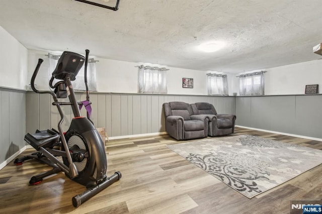 workout area featuring a wainscoted wall, a textured ceiling, and wood finished floors