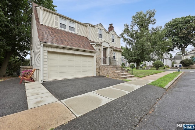 townhome / multi-family property with an attached garage, driveway, and roof with shingles