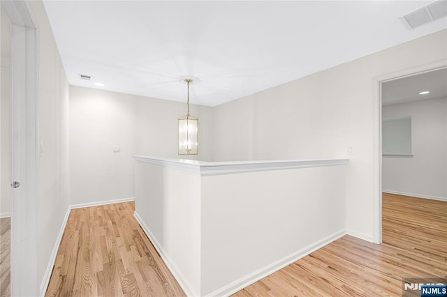 corridor featuring a chandelier, visible vents, light wood-type flooring, and baseboards