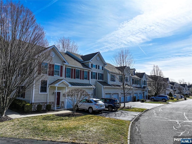 townhome / multi-family property with a residential view, a front yard, a garage, stone siding, and driveway