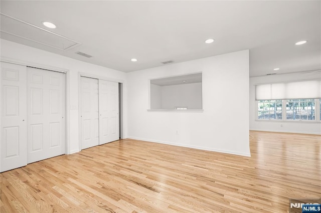 unfurnished bedroom with attic access, recessed lighting, wood finished floors, and two closets