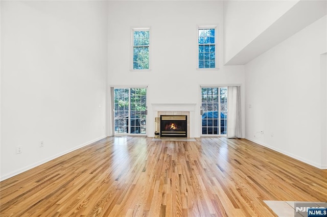 unfurnished living room featuring a fireplace with flush hearth, light wood-type flooring, baseboards, and a towering ceiling