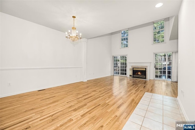 unfurnished living room featuring wood finished floors, visible vents, baseboards, a fireplace with flush hearth, and a chandelier