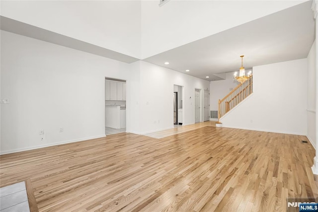 unfurnished living room featuring stairway, baseboards, a notable chandelier, and light wood-style flooring