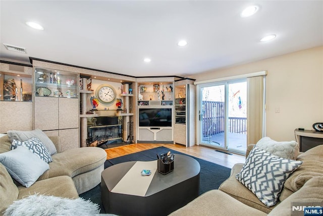 living room with recessed lighting, visible vents, wood finished floors, and a glass covered fireplace