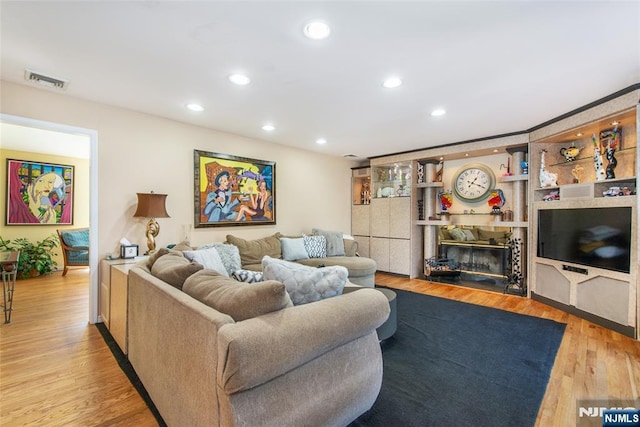 living area featuring a glass covered fireplace, visible vents, wood finished floors, and recessed lighting