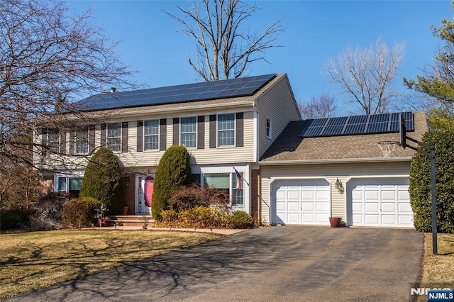 view of front of house with roof mounted solar panels, an attached garage, and driveway