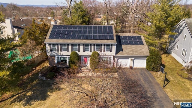 view of front of house featuring roof mounted solar panels, driveway, a chimney, and a garage