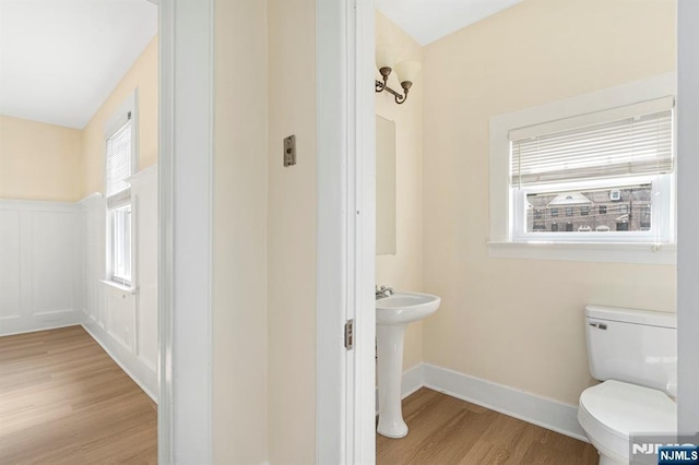 bathroom with plenty of natural light, toilet, a decorative wall, and wood finished floors