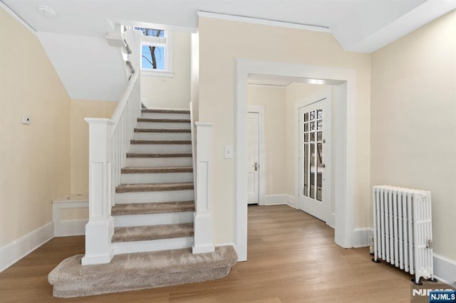 stairs featuring baseboards, radiator heating unit, lofted ceiling, and wood finished floors