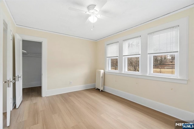 unfurnished bedroom with multiple windows, radiator, baseboards, and light wood finished floors