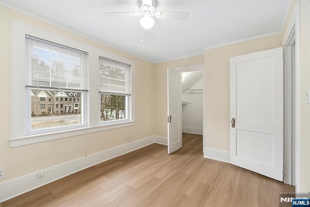 unfurnished bedroom featuring a spacious closet, crown molding, baseboards, light wood-style floors, and a closet