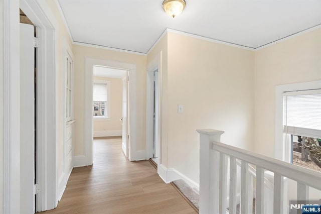 corridor featuring an upstairs landing, light wood-type flooring, baseboards, and ornamental molding