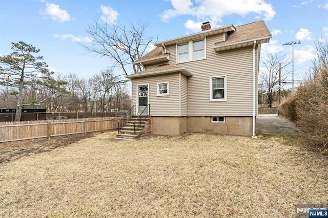 rear view of property with a shingled roof, fence, entry steps, a lawn, and a chimney