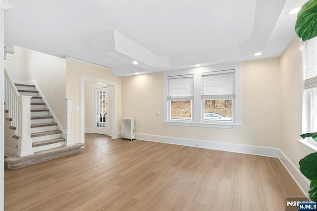 unfurnished living room with baseboards, light wood finished floors, radiator heating unit, recessed lighting, and a raised ceiling