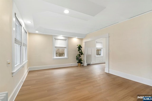 spare room featuring radiator, baseboards, recessed lighting, light wood-style floors, and a raised ceiling