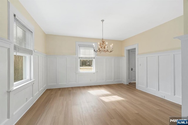 unfurnished dining area featuring a decorative wall, light wood-style floors, and an inviting chandelier