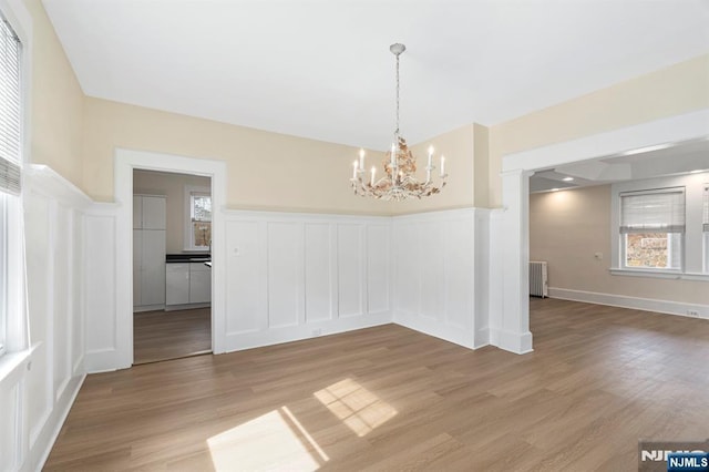 unfurnished dining area with an inviting chandelier, radiator heating unit, light wood-style floors, wainscoting, and a decorative wall