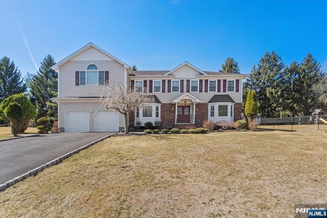 view of front facade with brick siding, a front lawn, fence, a garage, and driveway