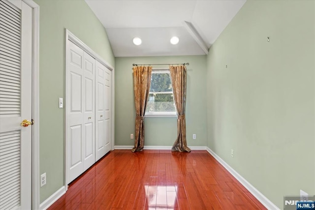 unfurnished bedroom featuring vaulted ceiling, wood finished floors, baseboards, and a closet