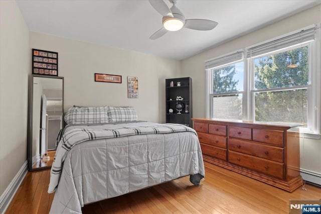 bedroom with baseboard heating, a ceiling fan, baseboards, and wood-type flooring