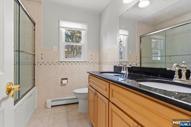 bathroom with a baseboard heating unit, tile walls, toilet, and a sink