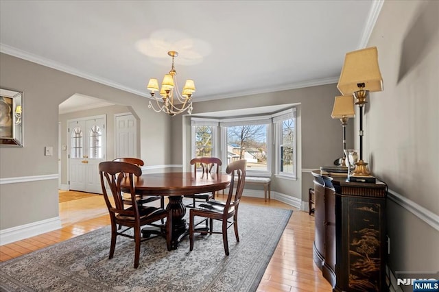 dining room with arched walkways, crown molding, light wood-style floors, and a wealth of natural light