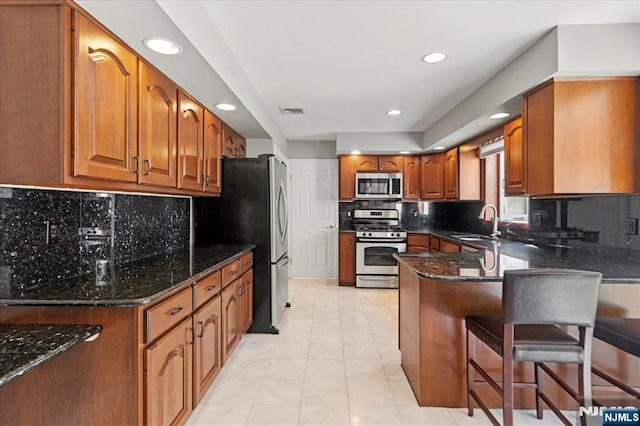 kitchen featuring visible vents, dark stone counters, a peninsula, brown cabinetry, and stainless steel appliances