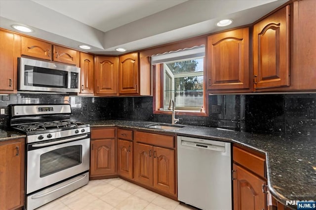 kitchen with a sink, stainless steel appliances, brown cabinetry, and dark stone counters