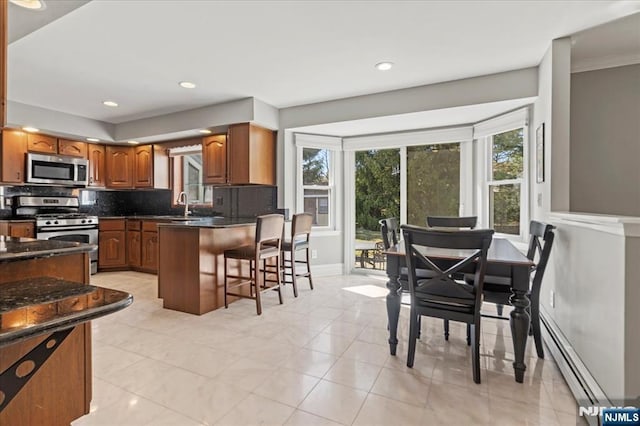 kitchen with a baseboard radiator, a peninsula, stainless steel appliances, decorative backsplash, and a kitchen bar