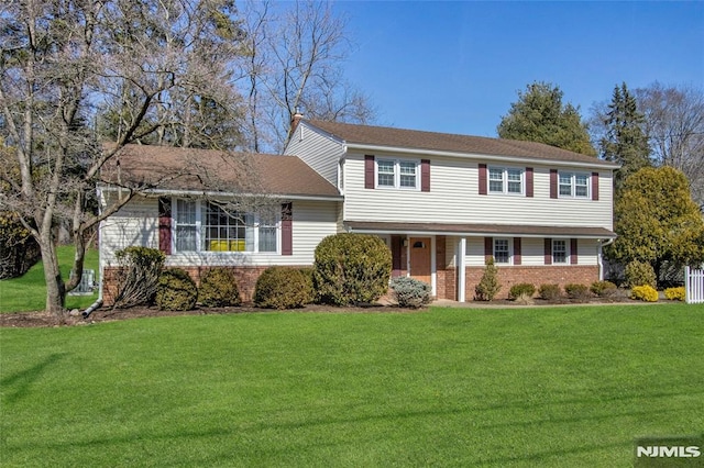 view of front of home with brick siding, a chimney, and a front yard