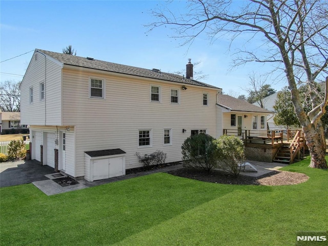 back of property featuring aphalt driveway, a yard, a wooden deck, a garage, and a chimney