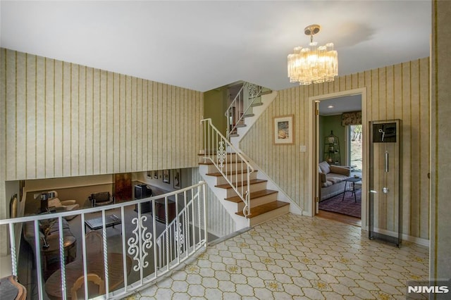 stairway with wallpapered walls, a notable chandelier, and baseboards