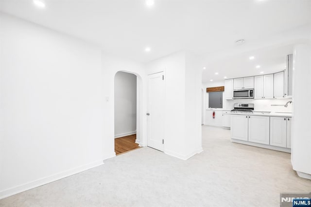 kitchen with baseboards, recessed lighting, arched walkways, a sink, and stainless steel appliances