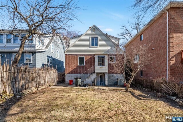 rear view of house with cooling unit, brick siding, a fenced backyard, and a lawn