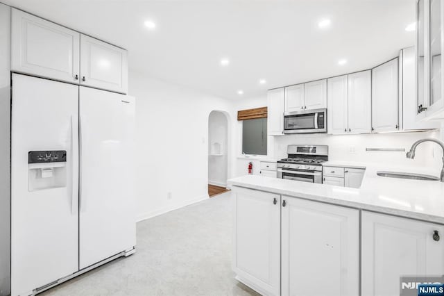 kitchen with a sink, arched walkways, appliances with stainless steel finishes, and white cabinetry