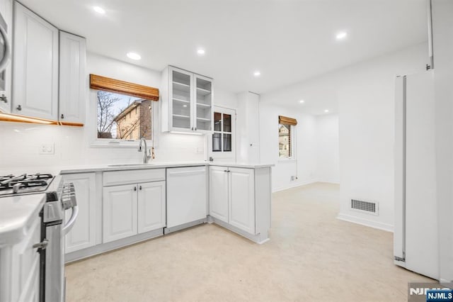 kitchen with tasteful backsplash, visible vents, white cabinets, white appliances, and a sink