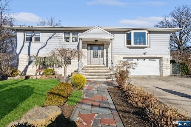 raised ranch with brick siding, concrete driveway, and an attached garage