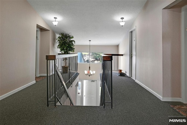 hallway with a textured ceiling, an upstairs landing, carpet floors, and a chandelier