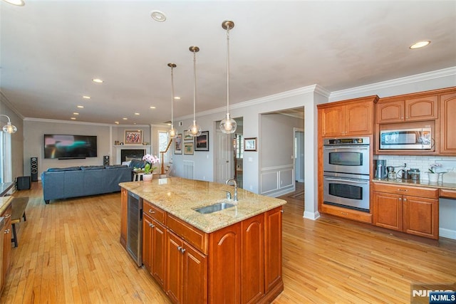 kitchen featuring wine cooler, a center island with sink, light wood-style floors, stainless steel appliances, and a sink