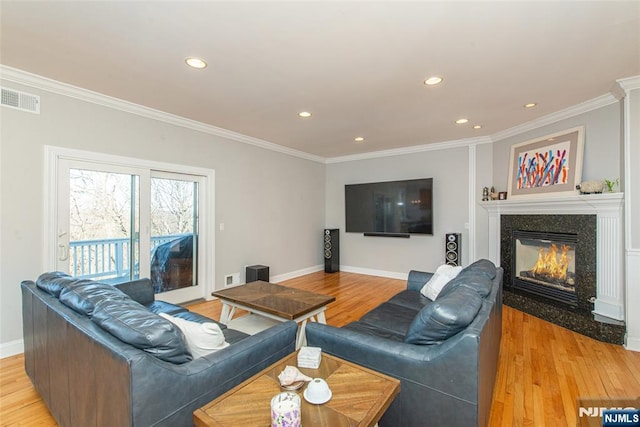 living room with a high end fireplace, visible vents, light wood finished floors, and ornamental molding