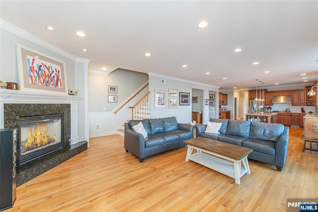 living room with stairs, crown molding, light wood finished floors, and a premium fireplace