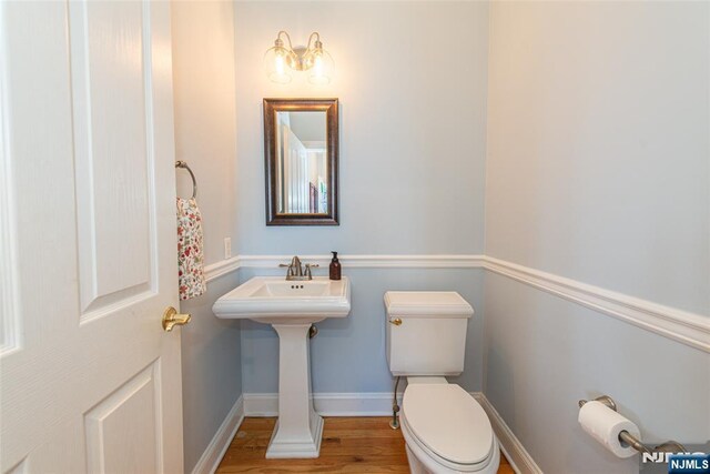 half bath with baseboards, toilet, and wood finished floors