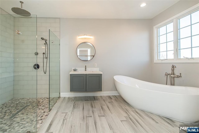 bathroom featuring vanity, wood finished floors, baseboards, tiled shower, and a soaking tub