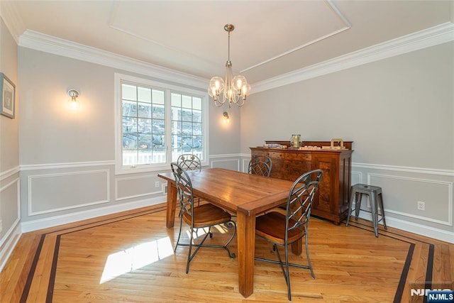 dining space with light wood-type flooring, a notable chandelier, wainscoting, and crown molding