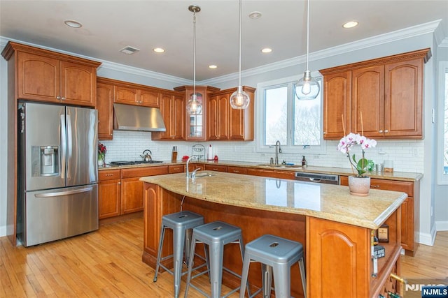 kitchen with under cabinet range hood, light wood-type flooring, brown cabinets, appliances with stainless steel finishes, and a sink