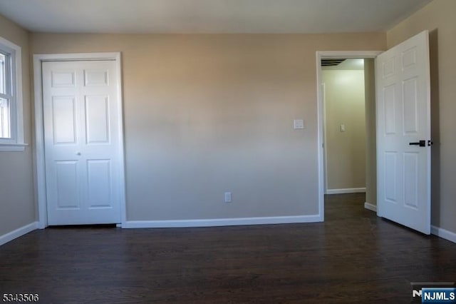 unfurnished bedroom with dark wood-style floors, baseboards, and a closet