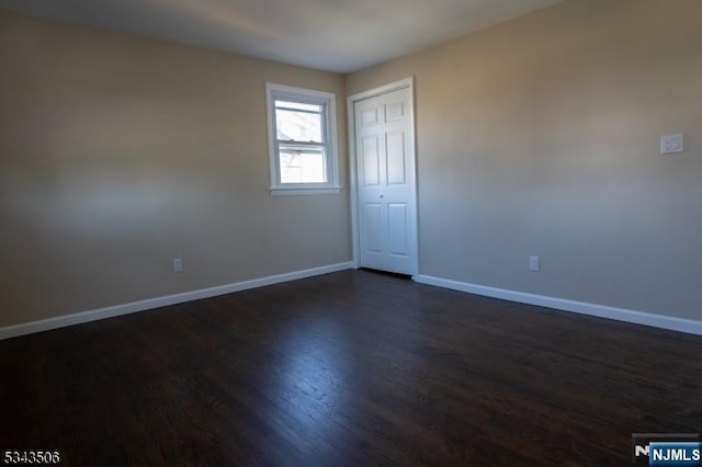 unfurnished room featuring baseboards and dark wood-type flooring